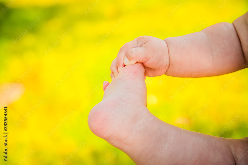 The baby is holding his foot with his hand on a yellow background of the gardenThe baby is holding his foot with his hand on a yellow background of the garden