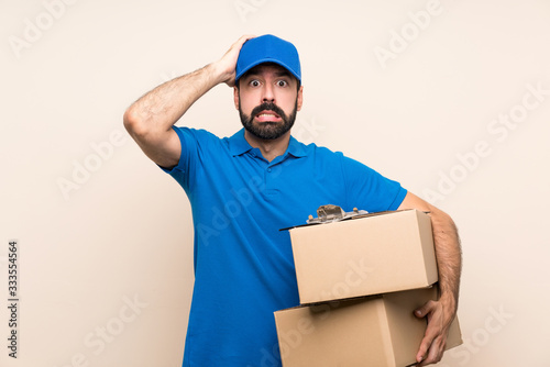 Delivery man with beard over isolated background frustrated and takes hands on head © luismolinero