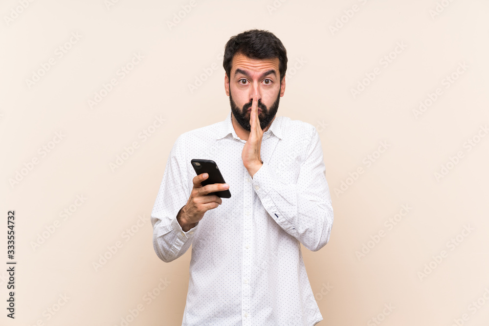 Young man with beard holding a mobile keeps palm together. Person asks for something Young man with beard holding a mobile keeps palm together. Person asks for something