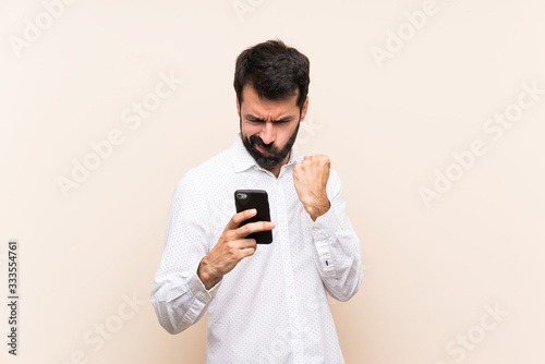 Young man with beard holding a mobile with angry gesture © luismolinero