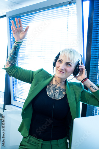 ragazza bionda tatuata con giacca verde ascolata muscia con le cuffie nel suo ufficio photo