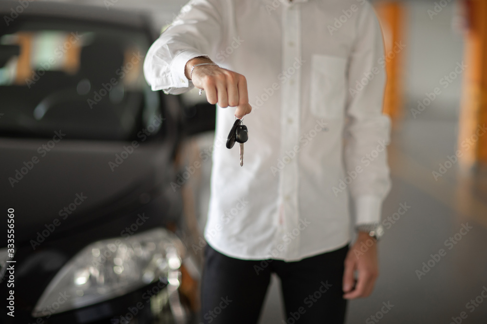 male hand holds car keys in front of him. background is white shirt and black car male hand holds car keys in front of him. background is white shirt and black car