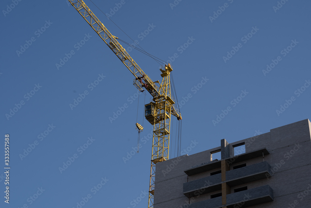 Modern building under construction with crane. From below of constructing building with high crane under clear sky Modern building under construction with crane. From below of constructing building with high crane under clear sky