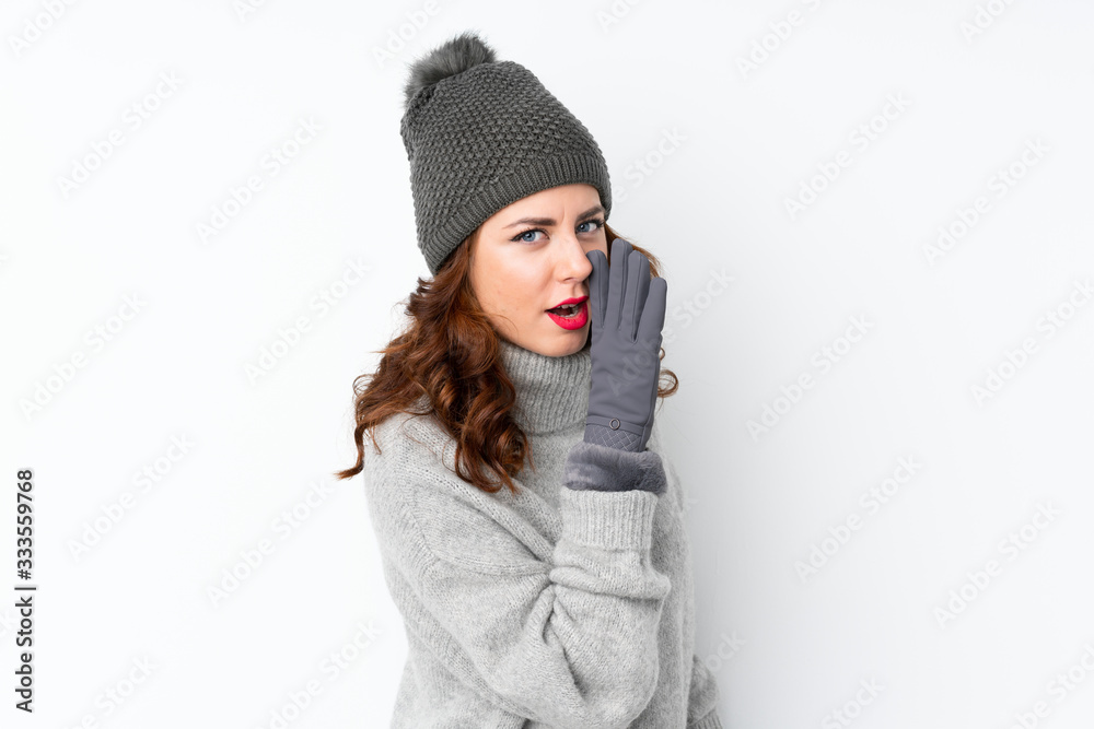Young Russian woman with winter hat over isolated white background whispering something