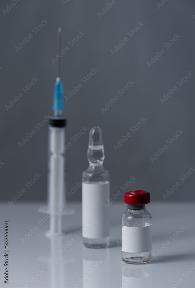 Medical vials for injection and a syringe, on gray background