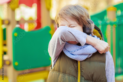 Schoolboy sneezing on arm elbow outdoor for protect from coronavirus photo