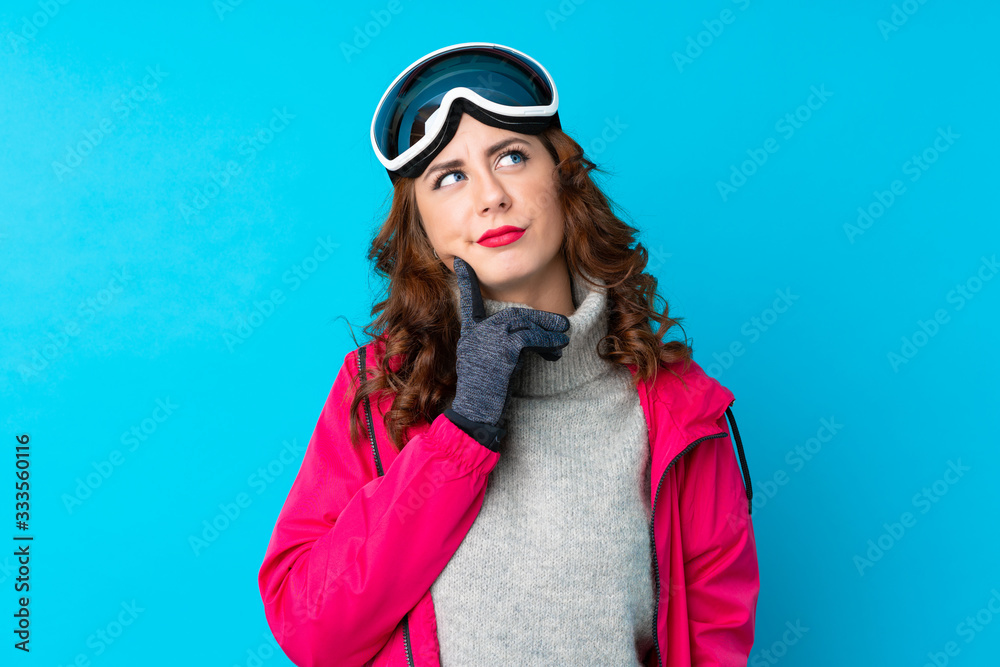 Skier woman with snowboarding glasses over isolated blue wall thinking an idea Skier woman with snowboarding glasses over isolated blue wall thinking an idea