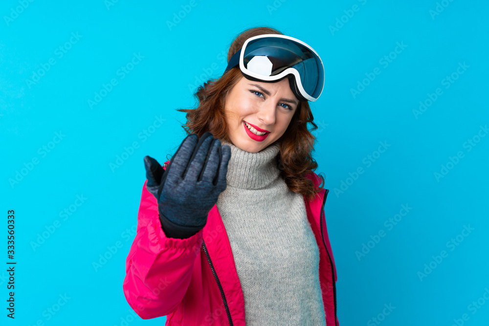 Skier woman with snowboarding glasses over isolated blue wall inviting to come