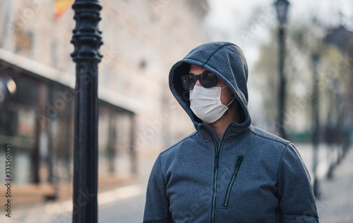 portrait of a brunette man in a surgical dressing and black glasses against the backdrop of a modern building, coronavirus, disease, infection, quarantine, medical mask