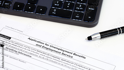 Application for employment benefits form with computer keyboard and pen on white background. Unemployment rate has risen sharply in United States due to closed business caused by corona virus outbreak