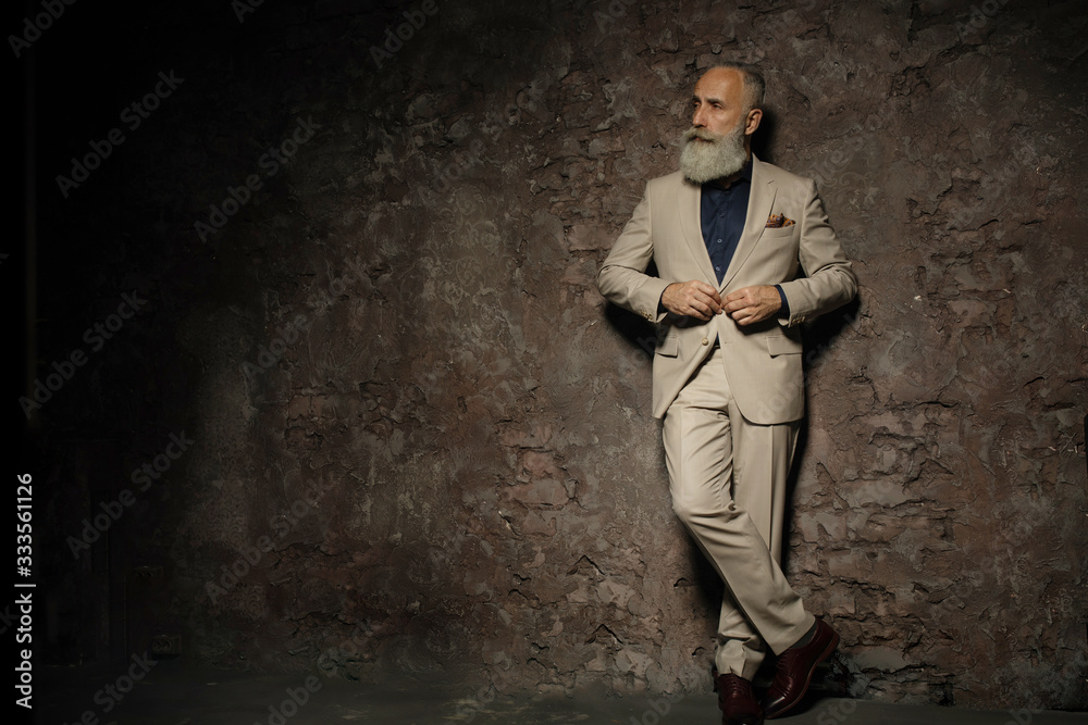 Portrait of adult businessman wearing trendy suit. Well-dressed bearded senior man in luxury interior.