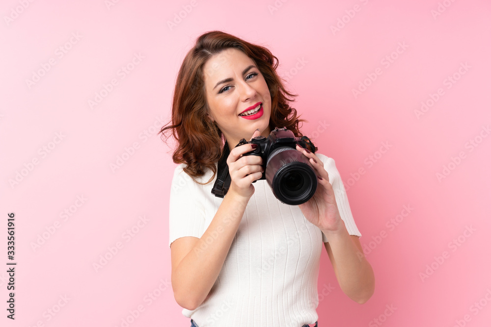 Obraz premium Young Russian woman over isolated pink background with a professional camera