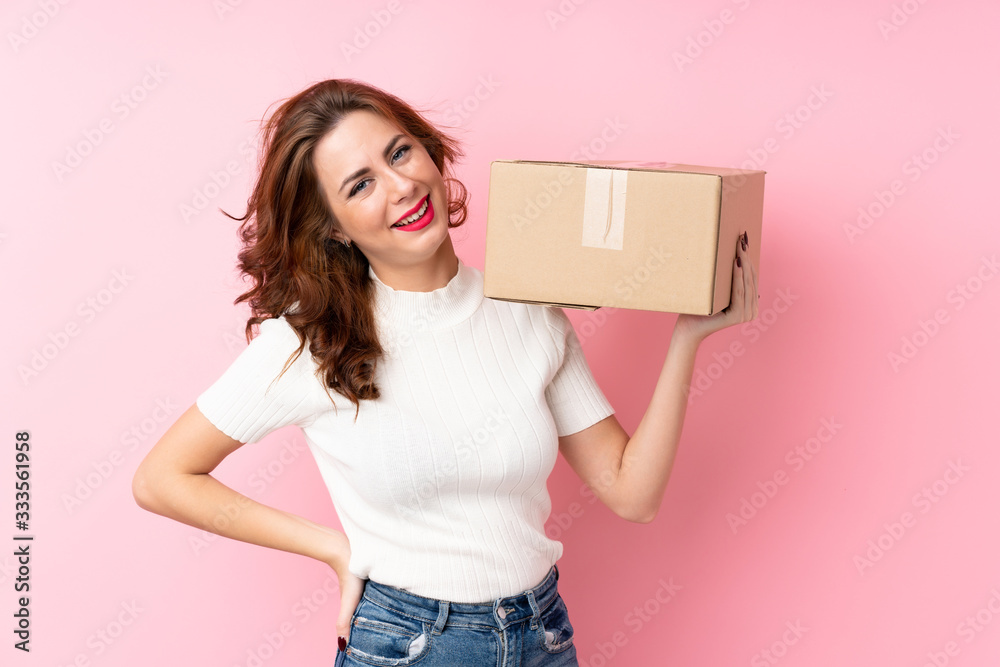 Young Russian woman over isolated pink background holding a box to move it to another site