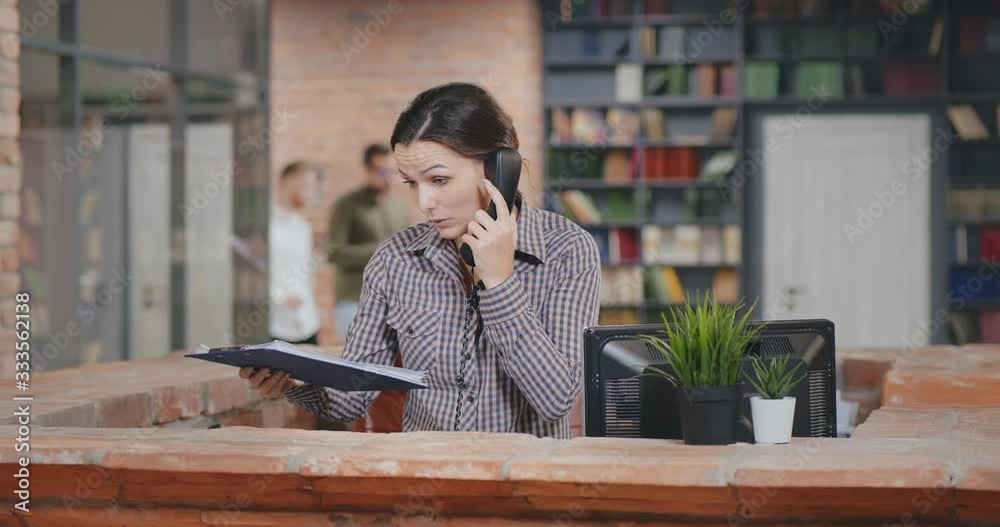 Secretary at reception desk consulting client on phone