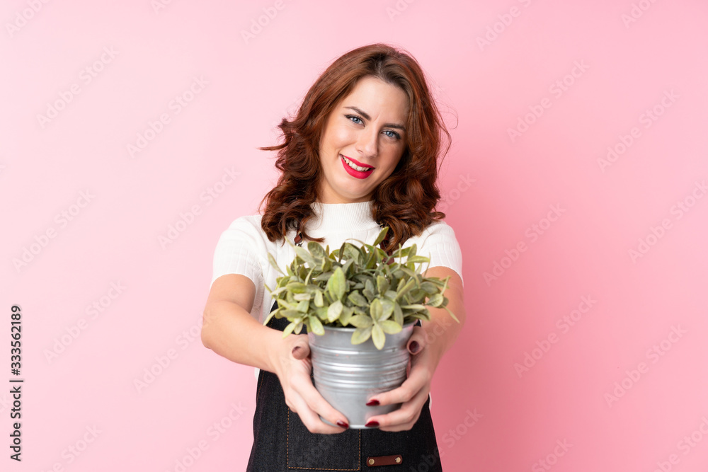 Young Russian woman over isolated pink background taking a flowerpot Young Russian woman over isolated pink background taking a flowerpot