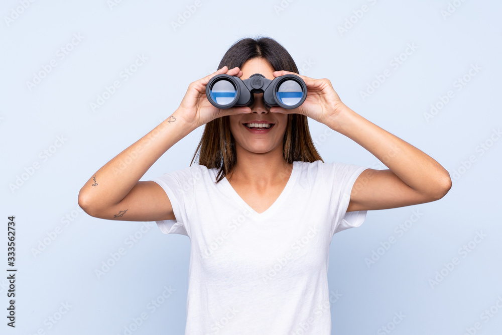 Young woman over isolated blue background with black binoculars Young woman over isolated blue background with black binoculars