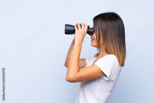 Young woman over isolated blue background with black binoculars