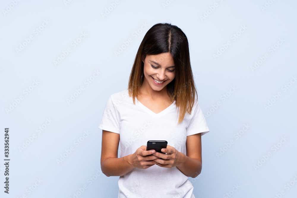 Young woman over isolated blue background sending a message or email with the mobile Young woman over isolated blue background sending a message or email with the mobile
