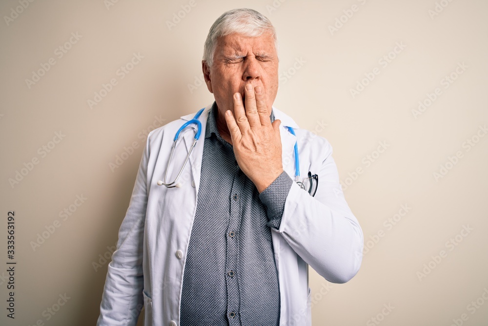 Senior handsome hoary doctor man wearing coat and stethoscope over white background bored yawning tired covering mouth with hand. Restless and sleepiness. Senior handsome hoary doctor man wearing coat and stethoscope over white background bored yawning tired covering mouth with hand. Restless and sleepiness.
