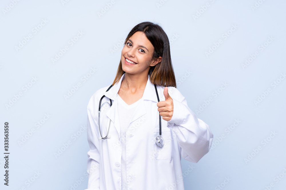 Young woman over isolated blue background with doctor gown and with thumb up Young woman over isolated blue background with doctor gown and with thumb up