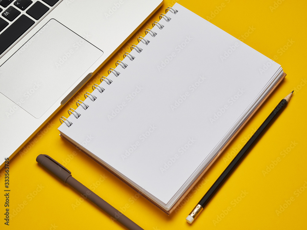 Workplace - laptop, notebook, pen, and pencil for remote work on a yellow background table. Freelance desktop for home or office. Background with copy space. Workplace - laptop, notebook, pen, and pencil for remote work on a yellow background table. Freelance desktop for home or office. Background with copy space.