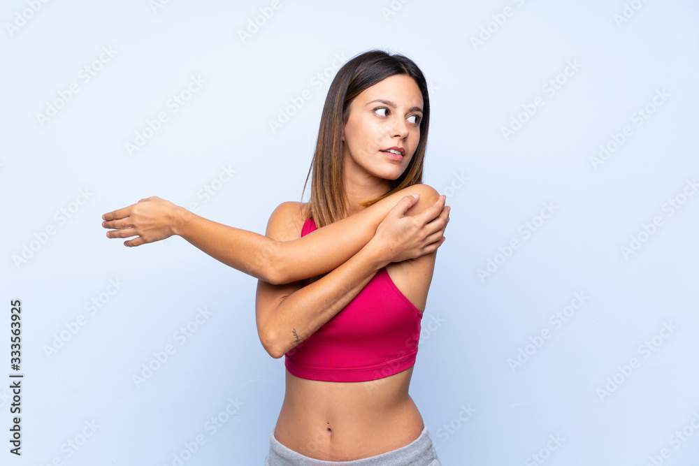 Young sport woman over isolated blue background stretching arm Young sport woman over isolated blue background stretching arm