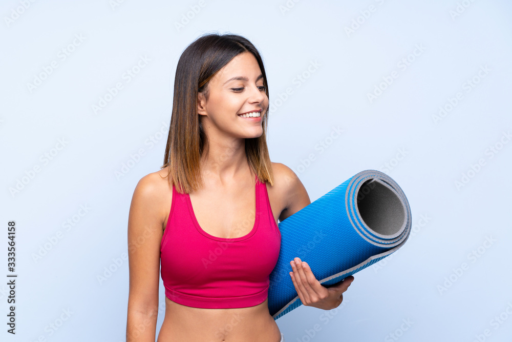 Young sport woman over isolated blue background with a mat Young sport woman over isolated blue background with a mat