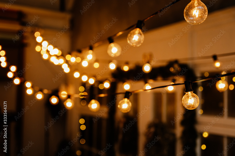 Luminous incandescent lamps hang in the form of a garland on wires, against the background of a shop window. Background from a garland. Incandescent lamps.
