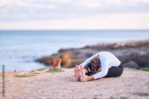 Young beautiful sportwoman practicing yoga. Coach teaching seated forward fold pose at the beach