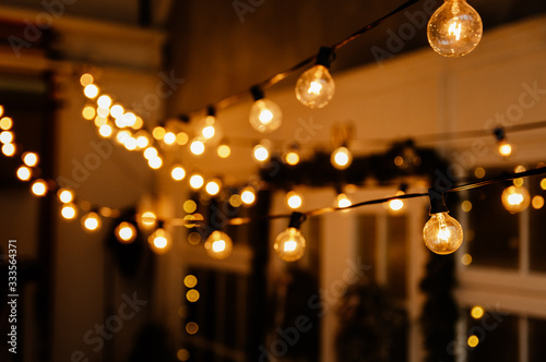 Luminous incandescent lamps hang in the form of a garland on wires, against the background of a shop window. Background from a garland. Incandescent lamps.