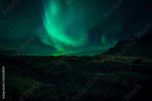 Image of Northern Lights illuminating the sky with a mountain landscape backdrop in Iceland during night time © Ernest