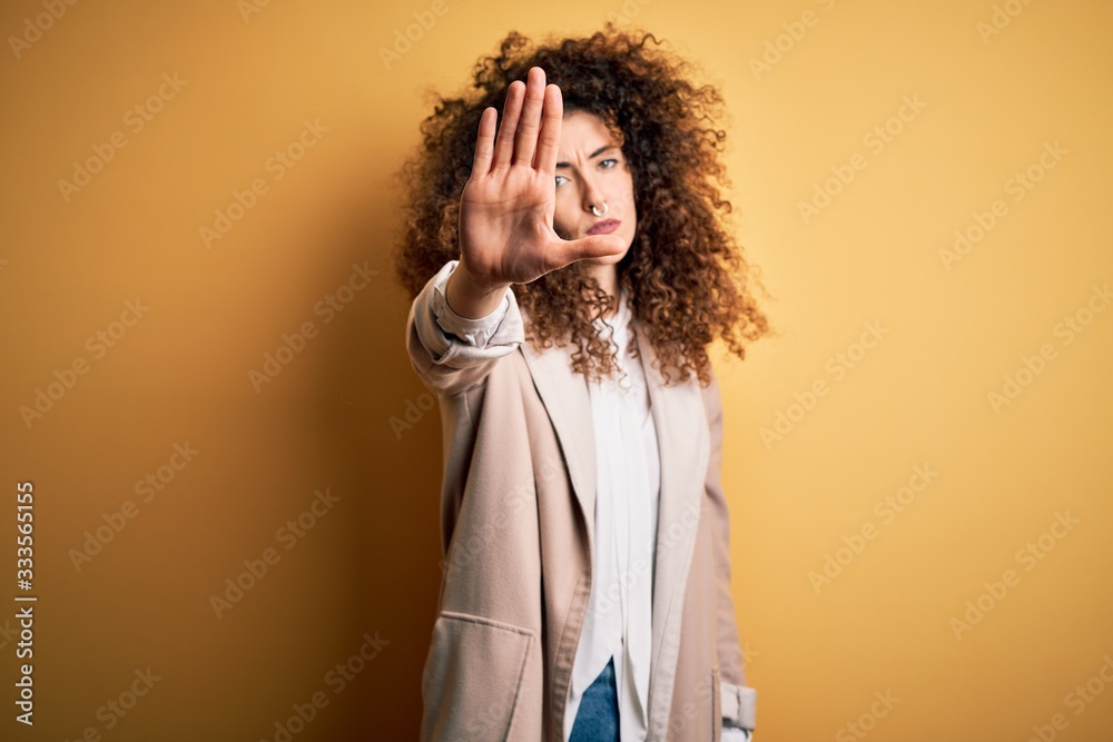 Young beautiful brunette woman with curly hair and piercing wearing casual t-shirt and diadem doing stop sing with palm of the hand. Warning expression with negative and serious gesture on the face.