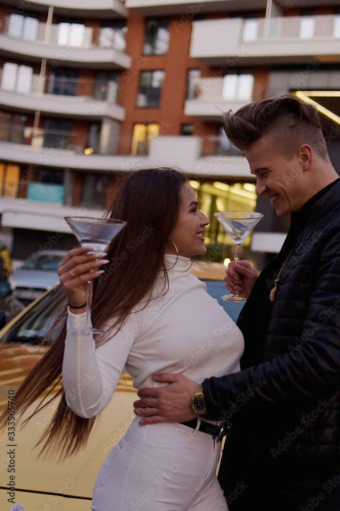 A couple of notes at night, drinking alcohol near a golden car. Gorgeous couple, rich people, have fun. A guy with a girl driving a car. Man in black, girl in white. A couple of notes at night, drinking alcohol near a golden car. Gorgeous couple, rich people, have fun. A guy with a girl driving a car. Man in black, girl in white.