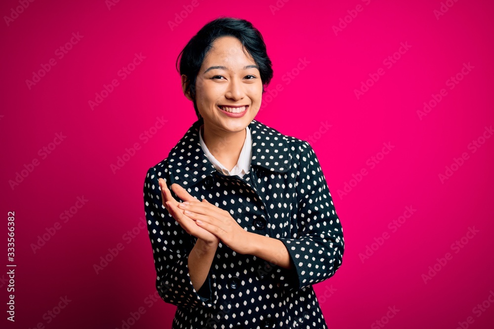 Young beautiful asian girl wearing casual jacket standing over isolated pink background clapping and applauding happy and joyful, smiling proud hands together