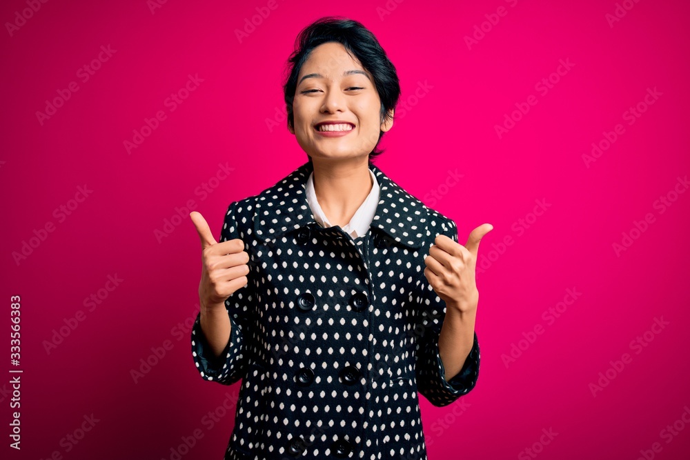 Young beautiful asian girl wearing casual jacket standing over isolated pink background success sign doing positive gesture with hand, thumbs up smiling and happy. Cheerful expression and winner Young beautiful asian girl wearing casual jacket standing over isolated pink background success sign doing positive gesture with hand, thumbs up smiling and happy. Cheerful expression and winner