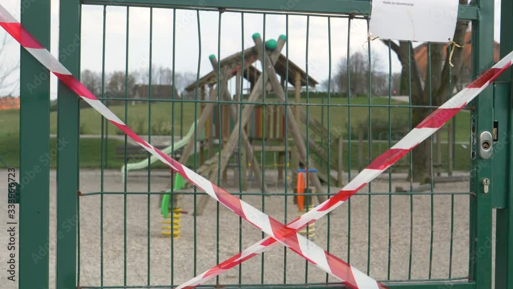 CLOSE UP, DOF: Red and white tape forbidding people to enter the kindergarten playground flutters in the wind. Entrance to a playground is locked and taped up due to the coronavirus epidemic in Europe CLOSE UP, DOF: Red and white tape forbidding people to enter the kindergarten playground flutters in the wind. Entrance to a playground is locked and taped up due to the coronavirus epidemic in Europe