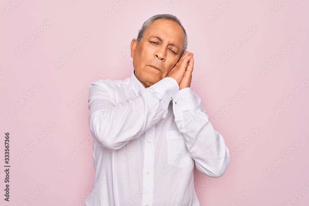 Senior handsome grey-haired man wearing elegant shirt over isolated pink background sleeping tired dreaming and posing with hands together while smiling with closed eyes. Senior handsome grey-haired man wearing elegant shirt over isolated pink background sleeping tired dreaming and posing with hands together while smiling with closed eyes.