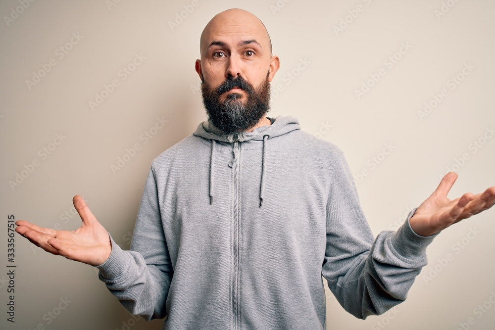 Handsome sporty bald man with beard wearing sweatshirt standing over pink background clueless and confused expression with arms and hands raised. Doubt concept. Handsome sporty bald man with beard wearing sweatshirt standing over pink background clueless and confused expression with arms and hands raised. Doubt concept.