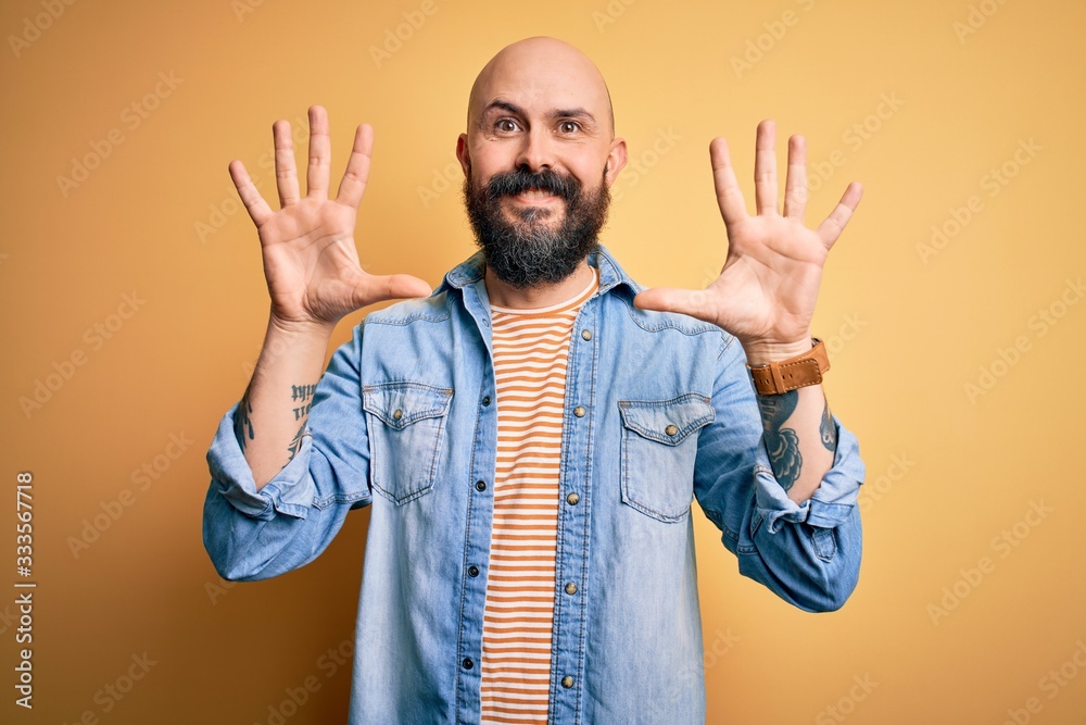 Handsome bald man with beard wearing casual denim jacket and striped t-shirt showing and pointing up with fingers number ten while smiling confident and happy. Handsome bald man with beard wearing casual denim jacket and striped t-shirt showing and pointing up with fingers number ten while smiling confident and happy.