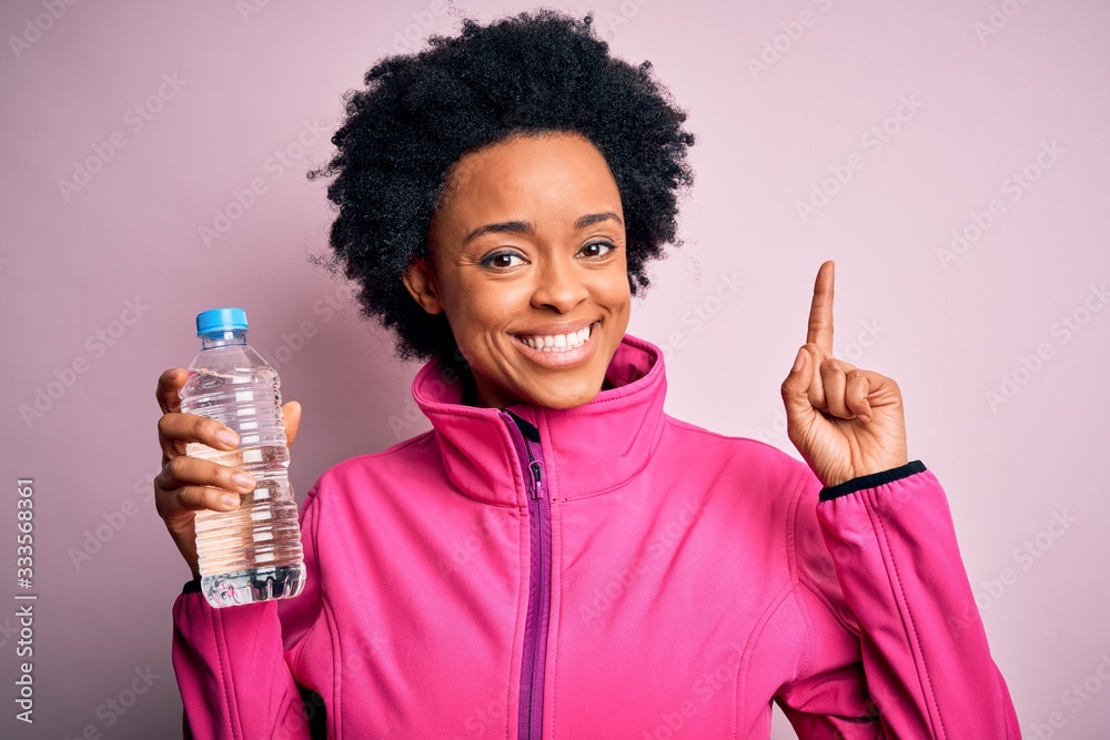 Young African American afro sportswoman with curly hair drinking bottle of water surprised with an idea or question pointing finger with happy face, number one Young African American afro sportswoman with curly hair drinking bottle of water surprised with an idea or question pointing finger with happy face, number one
