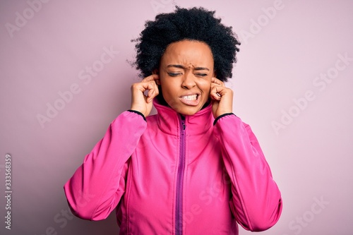 Young African American afro sportswoman with curly hair wearing sportswear doin sport covering ears with fingers with annoyed expression for the noise of loud music. Deaf concept.