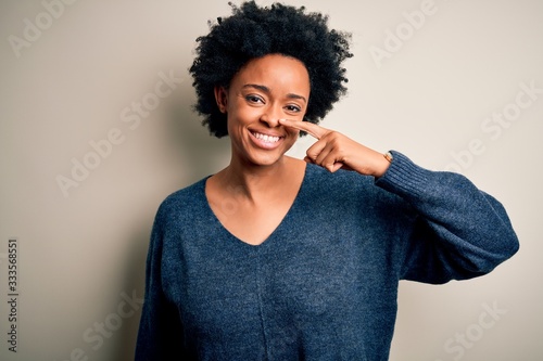 Young beautiful African American afro woman with curly hair wearing casual sweater Pointing with hand finger to face and nose, smiling cheerful. Beauty concept