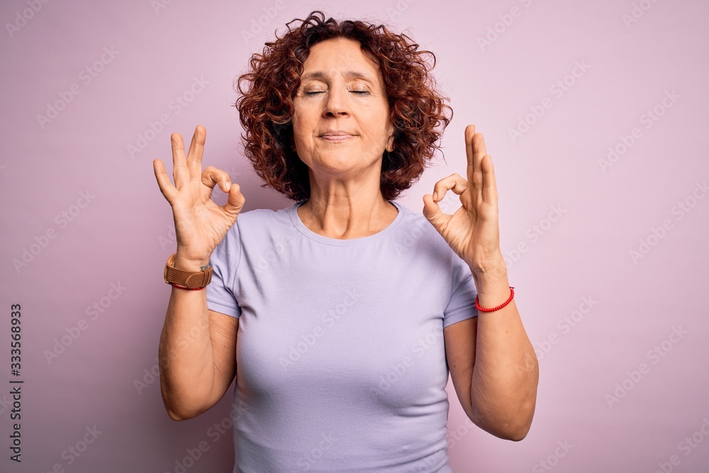 Middle age beautiful curly hair woman wearing casual t-shirt over isolated pink background relax and smiling with eyes closed doing meditation gesture with fingers. Yoga concept. Middle age beautiful curly hair woman wearing casual t-shirt over isolated pink background relax and smiling with eyes closed doing meditation gesture with fingers. Yoga concept.