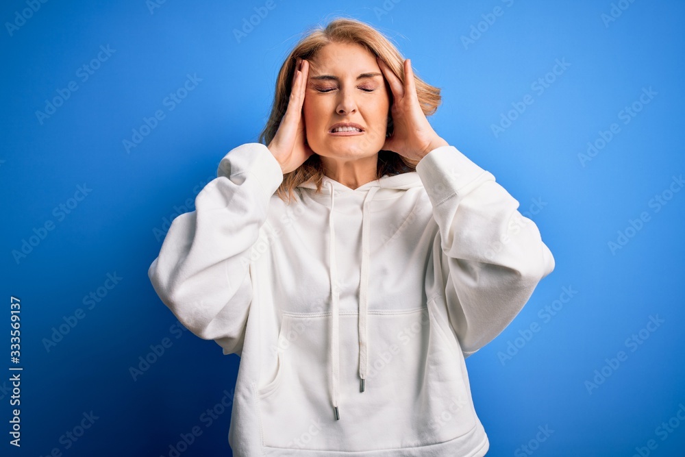 Middle age beautiful blonde sportswoman wearing sportswear over isolated blue background suffering from headache desperate and stressed because pain and migraine. Hands on head. Middle age beautiful blonde sportswoman wearing sportswear over isolated blue background suffering from headache desperate and stressed because pain and migraine. Hands on head.