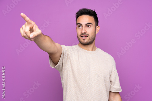 Young handsome man over isolated purple background pointing away