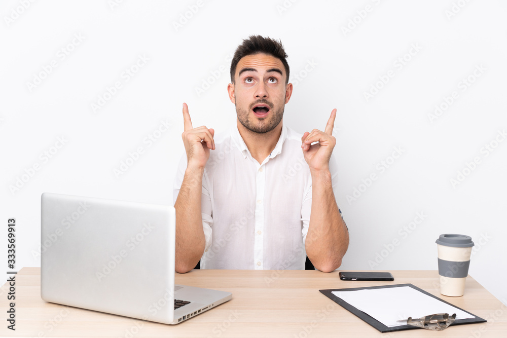 Young business man with a mobile phone in a workplace pointing with the index finger a great idea Young business man with a mobile phone in a workplace pointing with the index finger a great idea