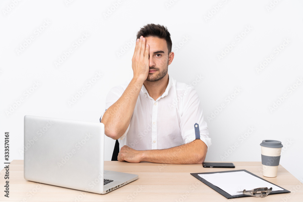 Young business man with a mobile phone in a workplace covering a eye by hand Young business man with a mobile phone in a workplace covering a eye by hand