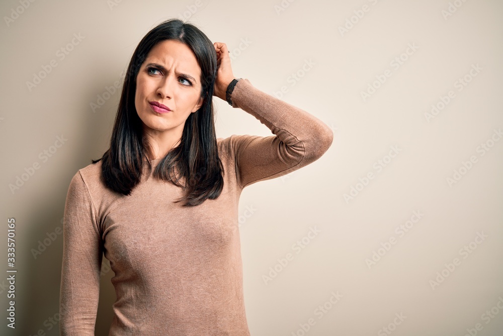 Fototapeta premium Young brunette woman with blue eyes wearing casual sweater over isolated white background confuse and wondering about question. Uncertain with doubt, thinking with hand on head. Pensive concept.