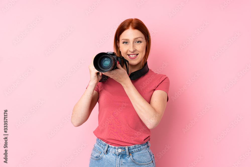 Obraz premium Young redhead woman over isolated pink background with a professional camera