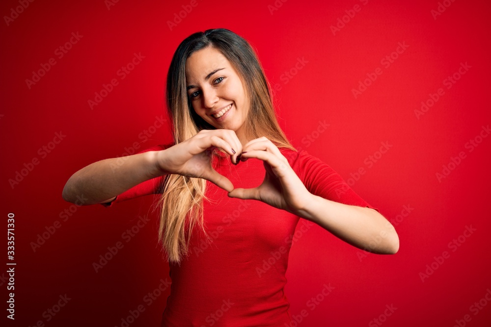 Young beautiful blonde woman with blue eyes wearing casual t-shirt over red background smiling in love doing heart symbol shape with hands. Romantic concept. Young beautiful blonde woman with blue eyes wearing casual t-shirt over red background smiling in love doing heart symbol shape with hands. Romantic concept.